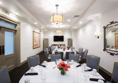 Three round tables with blue chairs around them sit in a private dining room space. THe tables have brightly colored floral displays and coffee mugs sit on the tables.