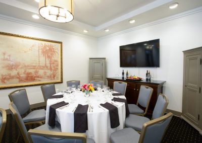 A round table with blue chairs around them sit in a private dining room space. THe tables have brightly colored floral displays and coffee mugs sit on the tables.