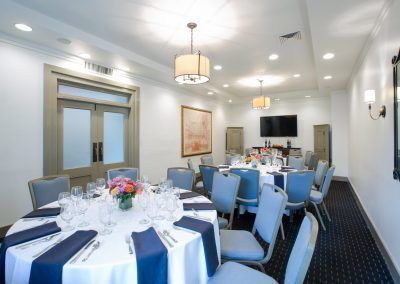 Three round tables with blue chairs around them sit in a private dining room space. THe tables have brightly colored floral displays and coffee mugs sit on the tables.