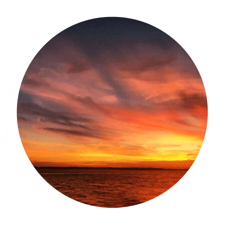 A sunset over the harbor shows a sky filled with yellows, orange, purples and blue hues