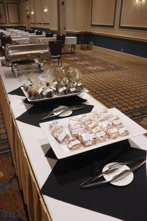 A long table with black and white tablecloths has two plates of wrapped food on them. A silver warming chaser sits at the end of the table.