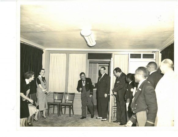 A man is walking into a room with a group of people laughing and smiling.