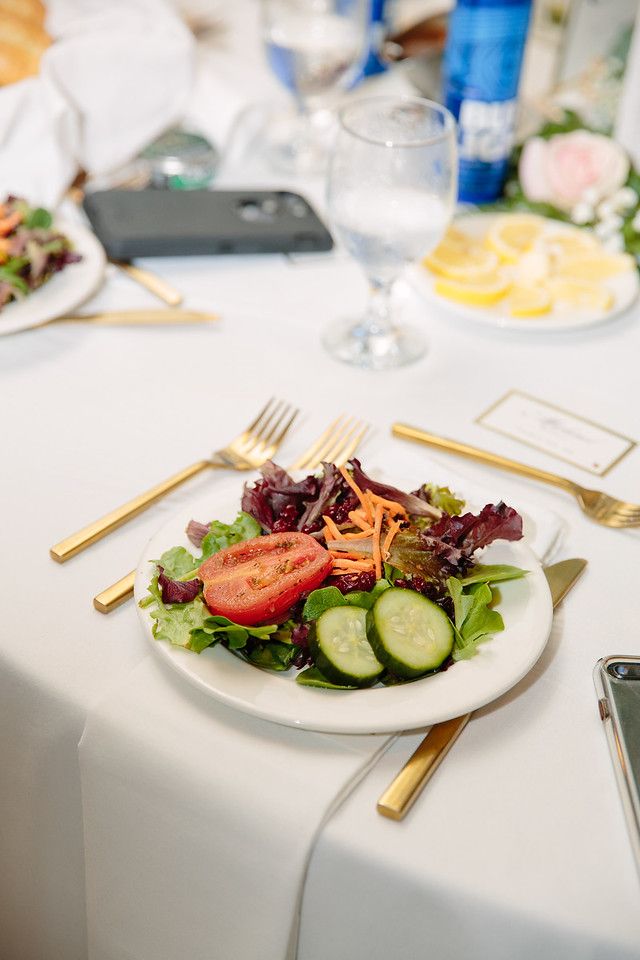 A small salad plate with gold utensils next to it sit on top of a table with a white tablecloth.