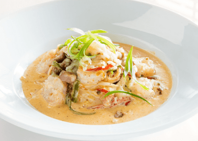 A bowl of shrimp and grits with a creamy orange sauce and green onions sit on top.