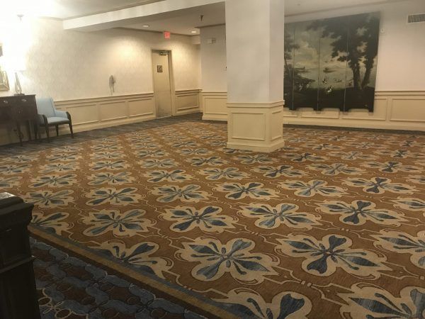 The pre function space of the gold ballroom consists of empty space to be used for many different events. blue and gold carpet line the floor and a painting of the marsh and trees is on the wall.