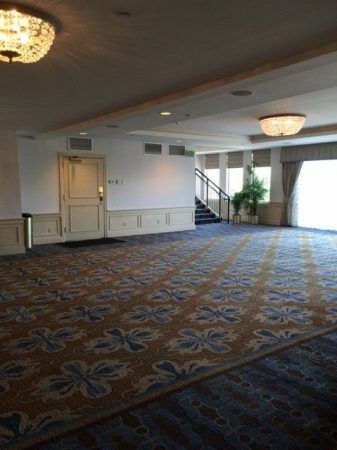 The pre function space of the Carolina ballroom consists of empty space to be used for many different events. Blue and gold carpet line the ground and bright chandeliers hang from the ceiling.