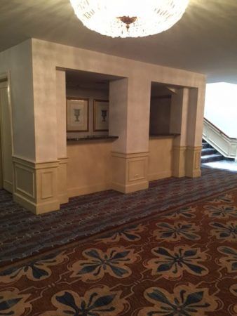 Two booths are in the center of the wall. Blue and gold carpet lines the ground and a staircase is to the right side.