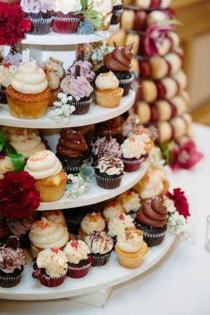 A close up of a cupcake display with a variety of colors. Reds, whites and dark brown cupcakes sit on a four tiered display shelf.