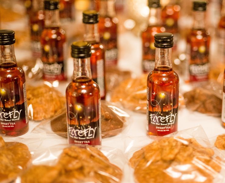 Firefly sweet tea mini bottles of vodka are grouped on a table and benne wafers lay next to them for a wedding favor.